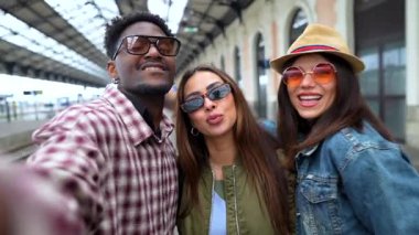 Ayrılık öncesi anıları yakalayan, gülümseyen ve ortak maceraya atılmadan önce hareketli tren istasyonunda grup selfie çeken bir grup neşeli arkadaş.