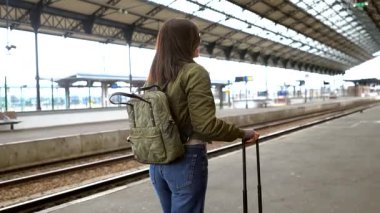 Tren peronunda yürüyen, tekerlekli bavulları çeken ve tren kalkana kadar akıllı telefonları kontrol eden bir yolcu.