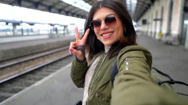 Tatil sırasında tren istasyonunda beklerken gülümseyen ve selfie çeken genç bir turist.