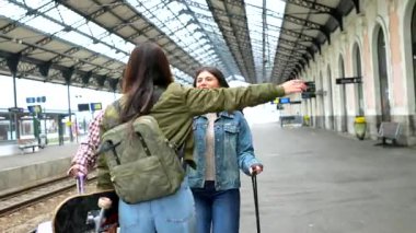 Tren istasyonunda toplanan arkadaşlar, neşeli kucaklaşmalar ve tren peronunun yakınındaki buluşmanın heyecanını paylaşıyorlar.