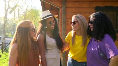 Farklı geçmişlere sahip, güneş gözlüğü takan, açık havada güneşli bir günde birlikte eğlenen, gerçek mutluluk ve dostluk saçan kadın arkadaşlar.