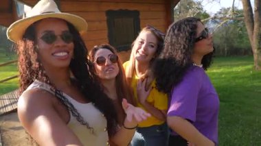 Dört farklı bayan arkadaş, tatillerinin tadını çıkarıyorlar, doğal ortamdaki ahşap bir kulübenin önünde selfie çekiyorlar.
