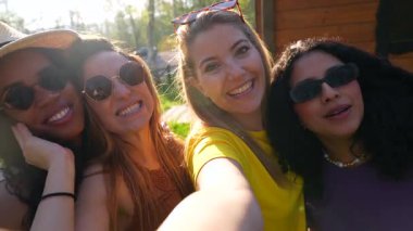 Neşeli çoklu etnik kadın arkadaşlar yaz anlarını yakalıyorlar, güneşli park ortamında neşeli selfie anıları yaratıp gerçek bağlantıları paylaşıyorlar.