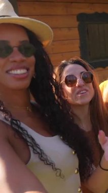 Çok ırklı bayan arkadaşlar birlikte vakit geçiriyorlar, selfie çekiyorlar ve ahşap bir evin önünde komik suratlar yapıyorlar.