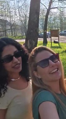 Güneşli park gününün tadını çıkaran, selfie çeken, kahkahalarını paylaşan ve kaygısız dostluk anları yaratan bayan arkadaşlar.