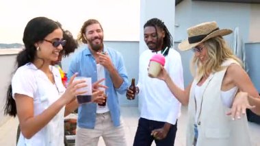 Kokteyllerle kaynaşan çok kültürlü arkadaşlar canlı çatı arkaplanı partisinde neşeyle dans ediyorlar.