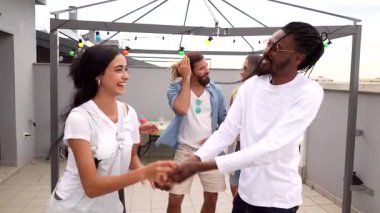 Enerjik genç arkadaşlar canlı çatı kutlamalarında neşeli anlar paylaşıyorlar, dans ediyorlar ve şehir ışıkları altında müzikle iletişim kuruyorlar.