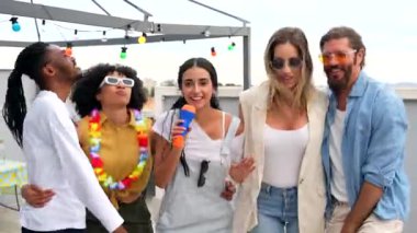 Çok kültürlü arkadaşlar karaoke yapıyor, şehir çatılarında gülüyor ve dans ediyorlar. Canlı bir yaz partisinde şehrin ufuk çizgisi arka planında.