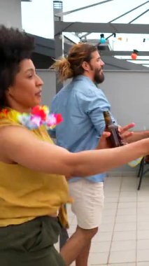 Çok kültürlü arkadaşlar içki paylaşıyor, dans ediyor ve şehir ışıkları altında canlı çatı kutlamaları sırasında unutulmaz bağlantılar kuruyorlar.