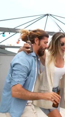 Çok kültürlü arkadaş grubu canlı çatı kutlamalarının tadını çıkarıyor, dans ediyor ve şehir silüetinin altında içkileri tokuşturuyor.