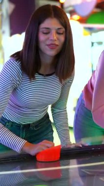 Arkadaşlar yaz heyecanını paylaşıyor, hava hokeyi maçında enerjik bir enerjiyle yarışırken atari salonunun atmosferinin tadını çıkarıyor, birlikte gülüyor ve oynuyorlar.