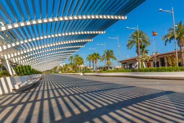 Çağdaş bir pergola boyunca süzülen güneş ışığı İspanyol gezinti alanında çarpıcı gölgeler yaratarak şehir manzarasına sanatsal bir dokunuş ekliyor.
