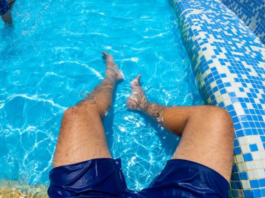Mavi bir yüzme havuzunda dinlenen güneşli bir yaz gününde ferahlatıcı suyun tadını çıkaran kaygısız bir tatil havasını kucaklayan bir adam.