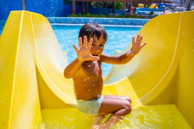 Eğlence parkında sarı su kaydırağından kayan mutlu çocuk yaz tatilinde eğleniyor.