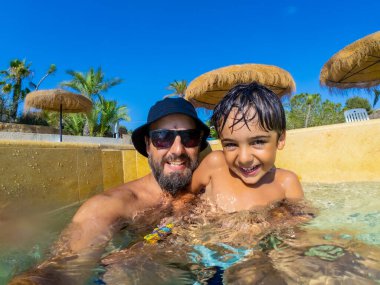 Mutlu baba ve oğul birlikte vakit geçiriyorlar, yaz tatilinde yüzme havuzunda oynuyorlar.