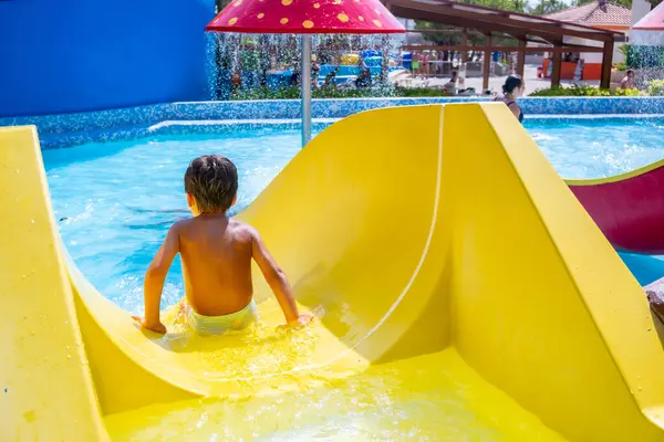 Genç bir çocuk, canlı bir su parkında canlı bir su kaydırağında yaz tatilinin heyecanını kucaklayarak heyecan verici bir yolculuğun tadını çıkarıyor.