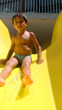 Genç çocuk yaz eğlencesini seviyor, parlak bir su kaydırağından kayıyor ve ferahlatıcı bir havuza sıçrıyor.