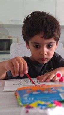 Anaokulu öğrencisi mutfak masasında güzel motor beceriler ve yaratıcılık geliştiren bir tablo çiziyor.