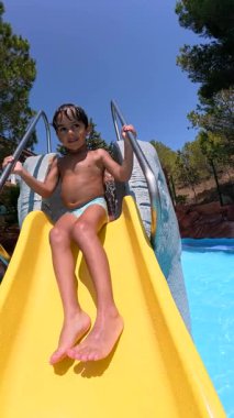 Heyecanlı bir çocuk güneşli bir günde su kaydırağından su birikintisine doğru eğlenceli bir yolculuk yapıyor. Su parkında saf eğlence ve macera.