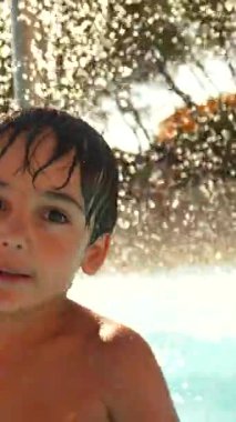 Neşeli genç çocuk su sıçratıyor, açık havuzda yaz tatili boyunca saf çocukluk mutluluğu yaşıyor.