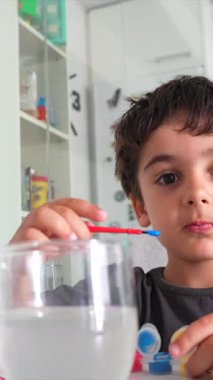 Genç bir çocuk suluboya resimlerini dikkatlice çiziyor, fırçasını bir bardak suya batırıyor.