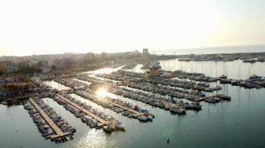 Altın gün doğumu, torrevieja marinasının sakin sularını yansıtarak limandaki tekneleri ve liman altyapısını ön plana çıkarıyor.