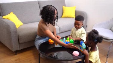 Anne, oğlu ve kızıyla etkileşime girer. Oturma odalarında renkli yapı taşlarıyla oynarlar.