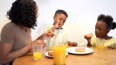 Afro-amerikan annesini seven tatlı çörek ve portakal suyunu mutlu çocuklarla paylaşan ev mutfağı masasındaki gevşetilmiş aile kahvaltısı sırasında