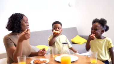 Çocukları besleyici sabah yemeklerini paylaşarak besleyen anneyi sevmek, aile kahvaltısı sırasında mutfakta sıcak bir bağ kurmak.