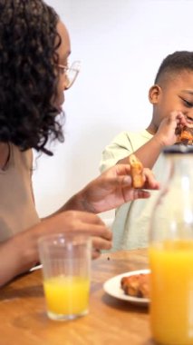 Aile evde sağlıklı bir kahvaltı yapıyor, anne ve küçük oğlu mutfakta kaynaşırken tatlı çörek ve taze portakal suyu paylaşıyorlar.