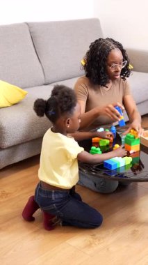 Anne ve çocuklar birlikte iyi vakit geçiriyorlar, oturma odasında renkli yapı taşlarıyla oynuyorlar.