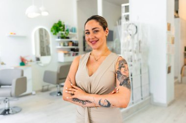 Modern güzellik salonunda kollarını kavuşturmuş gülümseyen bir kuaförün portresi. Gururlu küçük işletme sahibi.