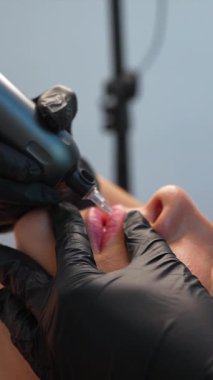 Profesyonel güzellik uzmanımız, steril güzellik salonu ortamında özel ekipmanlar kullanarak müşteriye dikkatlice dudak dövmesi yaptırıyor.