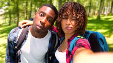 Genç yürüyüşçüler orman maceraları sırasında neşeli selfie anlarını paylaşıyorlar, yemyeşil orman manzarasını keşfederken neşeli bağlar ve spontane romantizm yakalıyorlar.