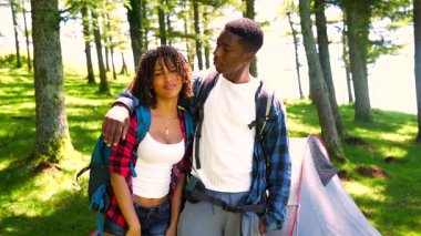 Genç Afrikalı Amerikalı gezginler, güneşli yaz maceraları boyunca yemyeşil ormanlarla çevrili bir şekilde kamp çadırının yanında mahrem bir anı paylaşıyorlar.