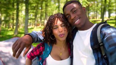 Mutlu genç bir çift ormanda kamp yaparken selfie çekiyor ve çadırlarının önünde komik suratlar yapıyor.