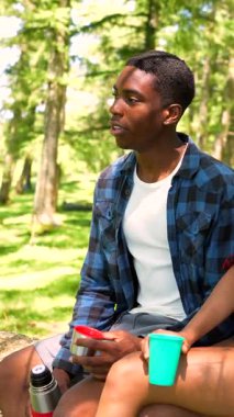 Genç siyah çift doğada dinleniyor, sohbet ediyorlar ve yeniden kullanılabilir bardaklardan içiyorlar.