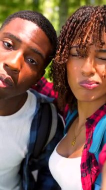 Genç Afro-Amerikan çifti neşeli selfie çekiyor, yaz tatili boyunca yemyeşil parkta neşeli anları yakalıyor, gülümsüyor ve otantik seyahat deneyimlerini paylaşıyorlar.