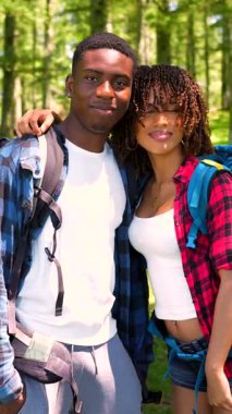 Genç yürüyüşçüler, yaz macerası boyunca yemyeşil ormanların ortasında durarak samimi bir anı paylaşıyorlar, kucaklaşıyorlar ve gülümsüyorlar.