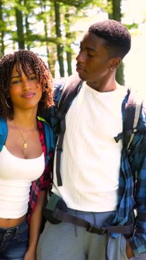 Genç yürüyüşçüler, yaz macerası boyunca yemyeşil orman manzarasının ortasında birbirlerine yakın durup neşe ve bağlarını ifade ederken sevgi dolu bir anı paylaşıyorlar.