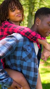 Romantik çift orman yürüyüşü sırasında neşeli anları paylaşıyor, yeşil ağaçlar ve yemyeşil bitki örtüsü arasında güneş ışığı altında gezintiye çıkıyorlar.