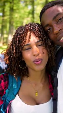 Neşeli çoklu etnik çiftler güneşli yaz maceraları sırasında yemyeşil ormanlarda yürürken neşeli selfie çekiyorlar.