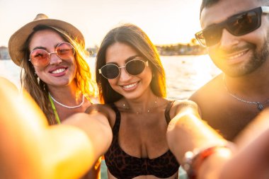 Neşeli genç arkadaşlar yaz tatillerinin tadını çıkarıyorlar, gün batımında eğlenceli bir selfie çekiyorlar.