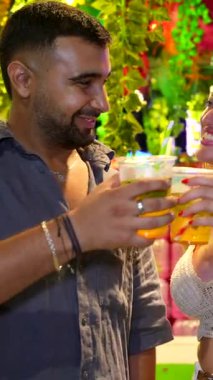 Genç çift canlı bir gece pazarında kokteyl içiyor, kutlama yapıyor ve birlikte eğleniyorlar.