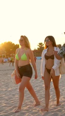 Bir grup genç arkadaş birlikte yürüyor, manzaralı sahil günbatımının tadını çıkarıyor, altın güneş ışığı ve rahat sahil titreşimleriyle kaygısız yaz tatili anları yakalıyorlar.