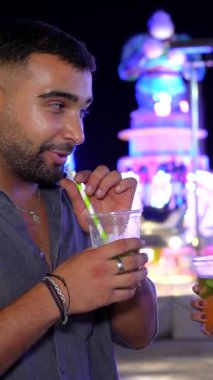 Çekici genç çift özel anları paylaşıyor, kokteyllerini yudumluyor ve birlikte gülüyorlar. Canlı eğlence parkında, mutluluk ve bağlantı yayıyorlar.