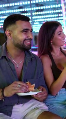 Genç arkadaşlar neşe dolu bir lunaparkta gülüşlerini ve hamburgerlerini paylaşıyorlar. Birlikte neşeli anılar yaratıyorlar.