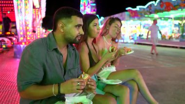 Genç bir çift, geceleri bir lunaparkta hamburger yiyor ve birlikte vakit geçiriyorlar.