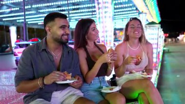 Neşeli bir lunaparkta, renkli ışıklarla aydınlatılmış hamburgerleri ve güzel zamanları paylaşan mutlu arkadaşlar.