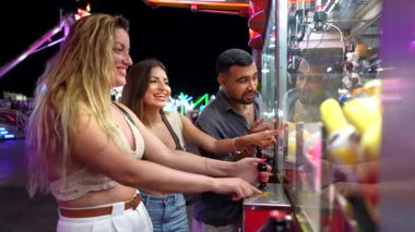 Gece yoldaşlığı, genç arkadaşlar eğlence parkında pençe turna oyunu oynarken kahkaha ve heyecan paylaşıyorlar.